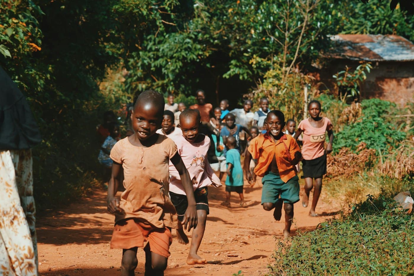 Children running along a red dirt path between trees