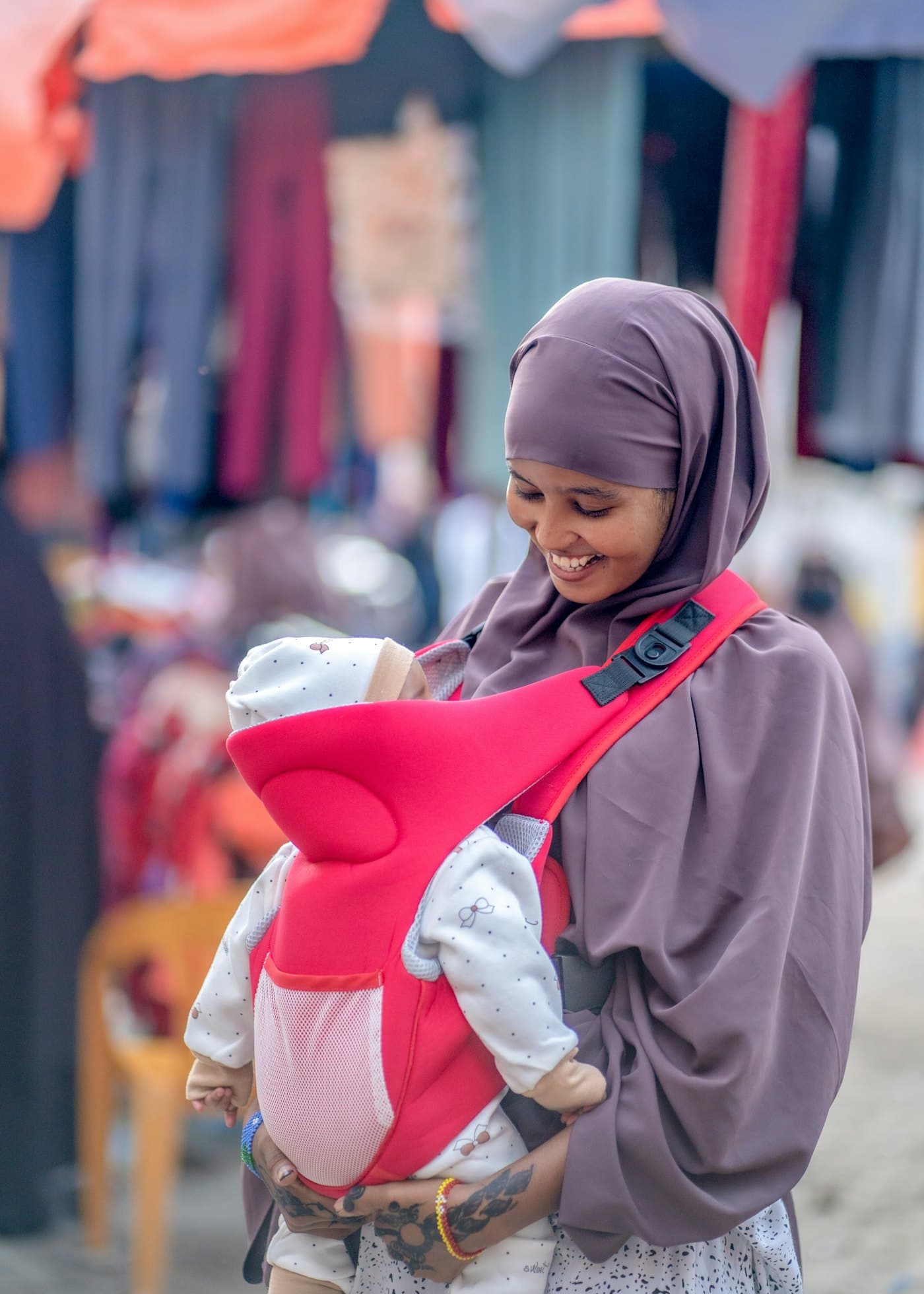 A smiling woman carrying her baby in a sling