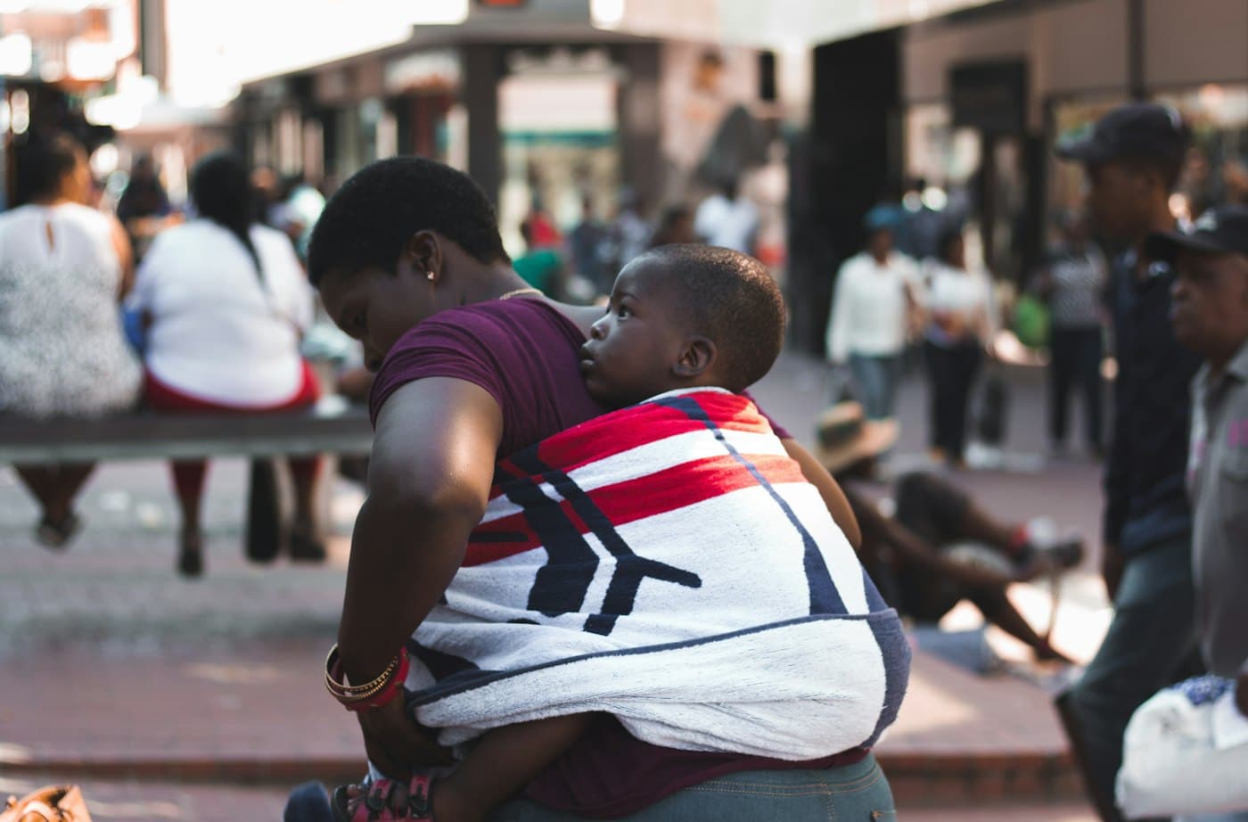 A woman in a busy street carrying a child on her back