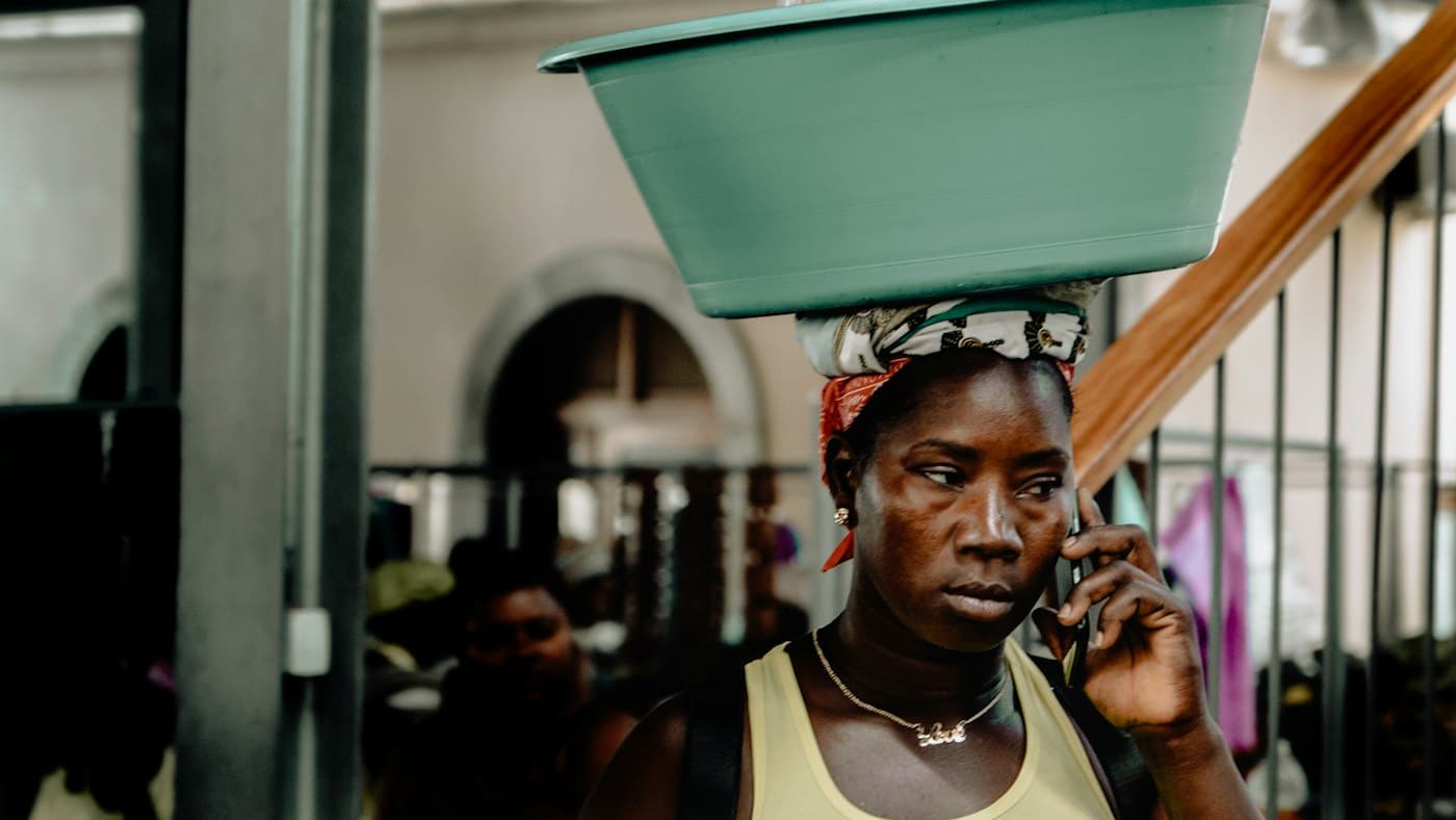 A woman with a basin on her head talking on a mobile phone