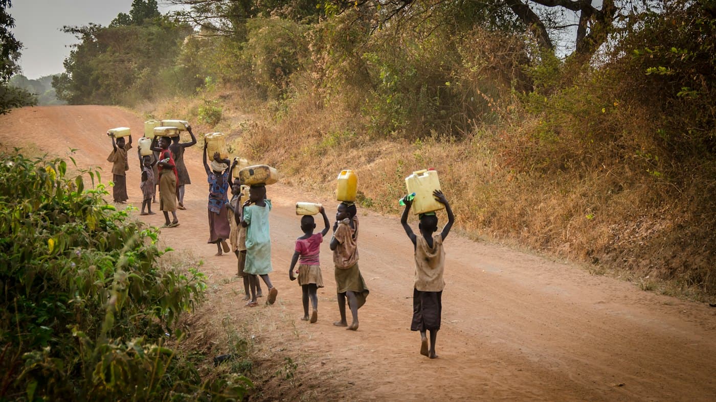 A line of people walking a dirt road carrying water containers